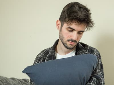 Depressed man hugging pillow looking down considering calling hotline
