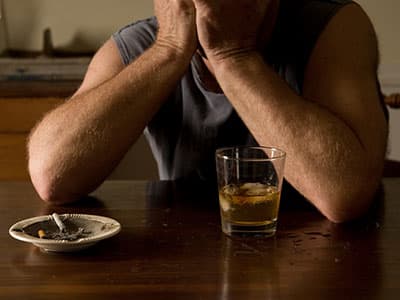 upset man with alcohol and cigarettes on table