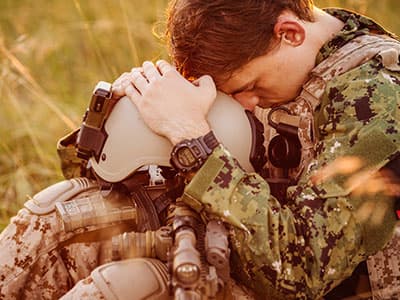 sad soldier sitting on ground holding helmet